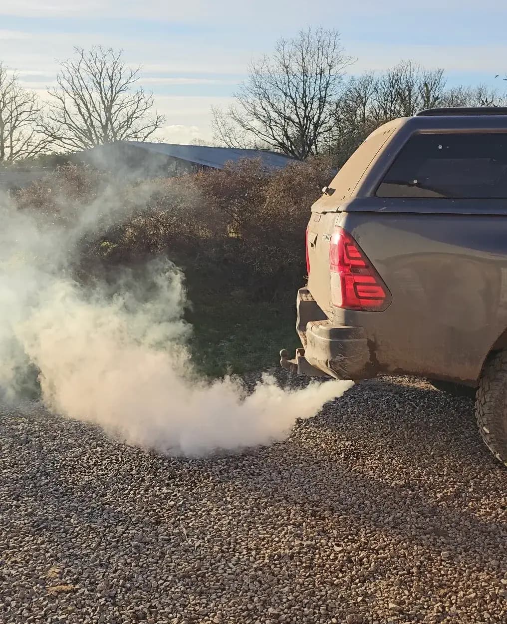 Toyota Hilux pickup on a gravel drive with a cloud of white smoke pouring from the exhaust during a DPF deep clean