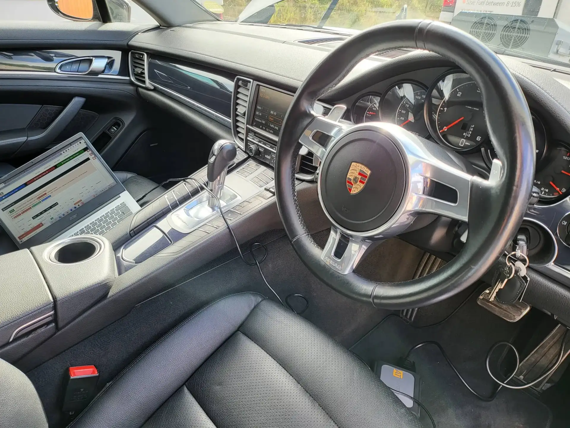 Porsche Panamera cabin during a gearbox (TCU) remap — laptop on the passenger seat, cable running past the PDK selector to the OBD port